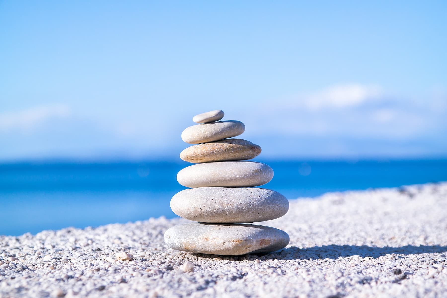 Rocks balanced on top of each other on a beach with a blue sky behind them